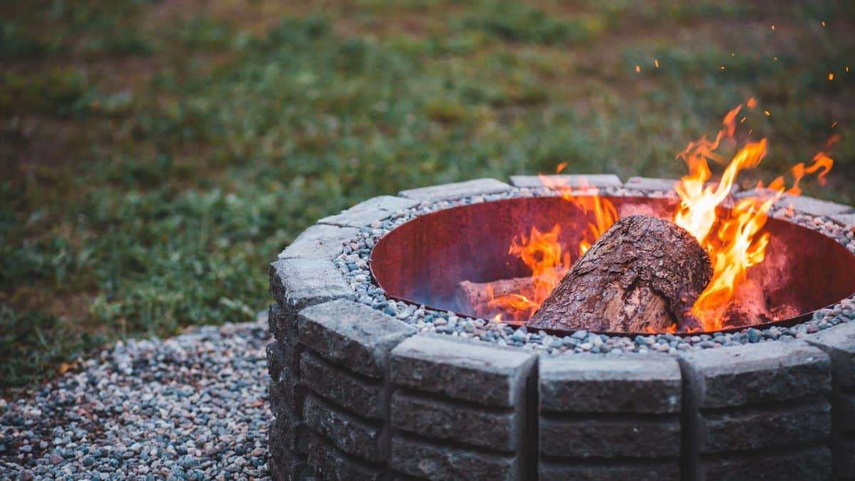 Bûche enflammée dans une vasque à feu ronde posée sur un sol couvert de galets